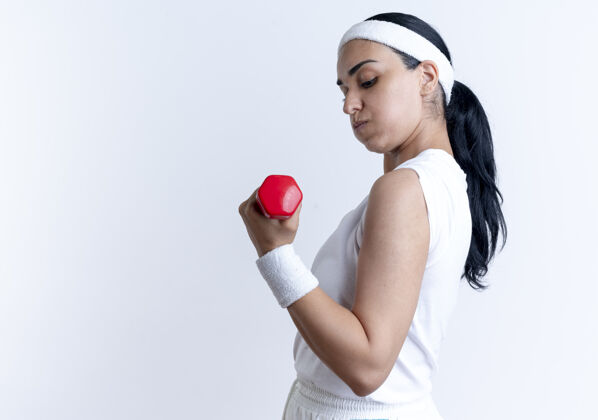 年轻年轻自信的白人运动女性戴着头带和腕带练习 看着哑铃孤立在白色空间与复制空间锻炼腕带哑铃