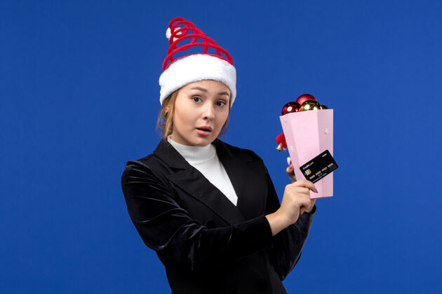 前面前视图年轻女士拿着银行卡在蓝色墙上新年情感节日玩具举行圣诞节人