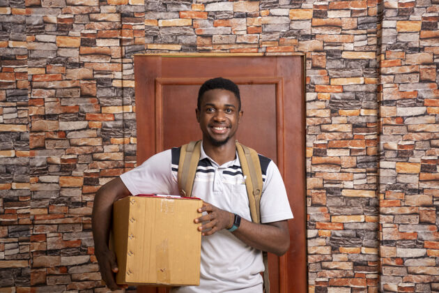 服务微笑的年轻非洲信使拿着包裹站在门前工作职业房子