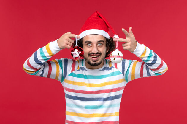 帽子正面图年轻男子手持圣诞树玩具在红墙新年红色假期肖像人前面