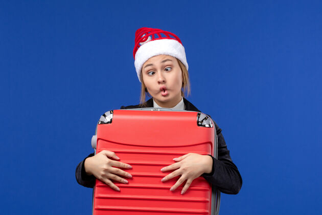 微笑正面图年轻女子提着沉重的红包在蓝色的墙上度假的女人度假圣诞节携带成人