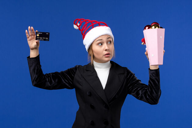 玩具前视图年轻女士拿着银行卡在蓝色墙上新年情绪节日玩具圣诞节看法专业