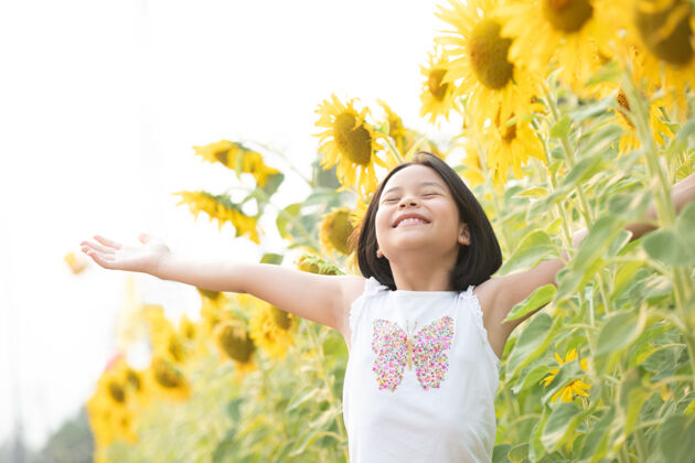 肖像快乐的亚洲小女孩在阳光下 在盛开的向日葵中嬉戏乐趣玩耍闻