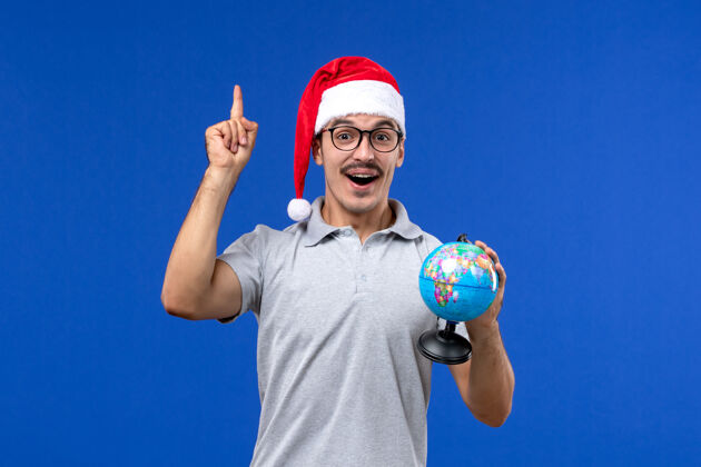 运动正面图年轻男性手持地球仪在蓝色地板上旅行人类飞机度假球员举行圣诞节