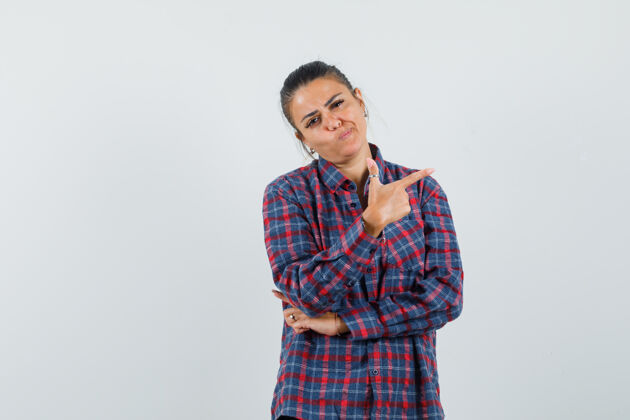 健康身穿格子衬衫的年轻女子用食指指着右边 面带沉思 正前方视图指着微笑手指