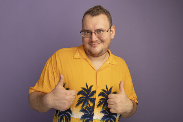眼镜一个戴着眼镜的男人穿着橘色衬衫站在紫色的墙上 开心而积极地竖起大拇指戴着大拇指男人