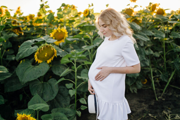 快乐一个穿着白裙子的金发女人在田里和向日葵在一起婴儿绿色妈妈