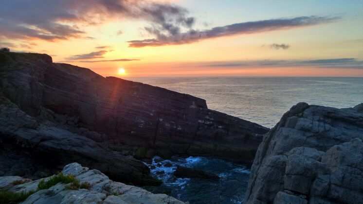 日落夕阳下的悬崖被海水包围平静光云