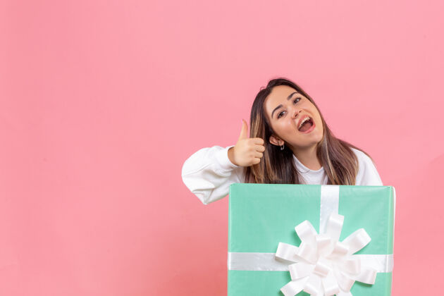 年轻女子正面图：年轻女子躲在礼物里 在粉色背景上微笑女性礼物成人