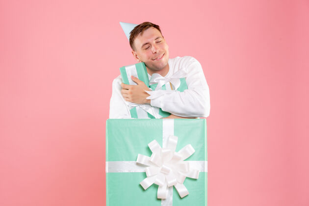 礼物正面图：年轻男性手持粉色背景的其他礼物圣诞成人微笑