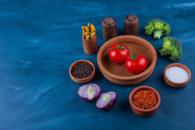 番茄把新鲜的西红柿 洋葱 西兰花和调味品放在蓝色的盘子里香料健康调味品