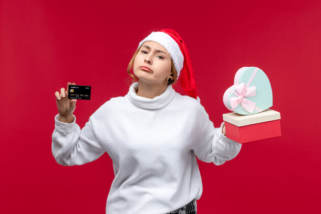 圣诞节正面图红色背景上的年轻女性 带着银行卡和礼物肖像卡片红色