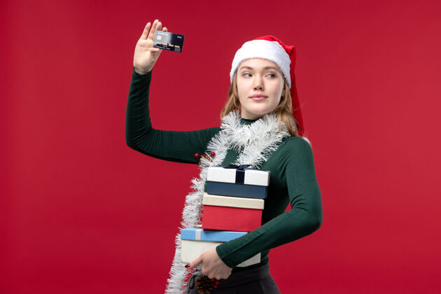 年轻女子正面图：手持礼物和红色背景的银行卡的年轻女子卡片正面肖像