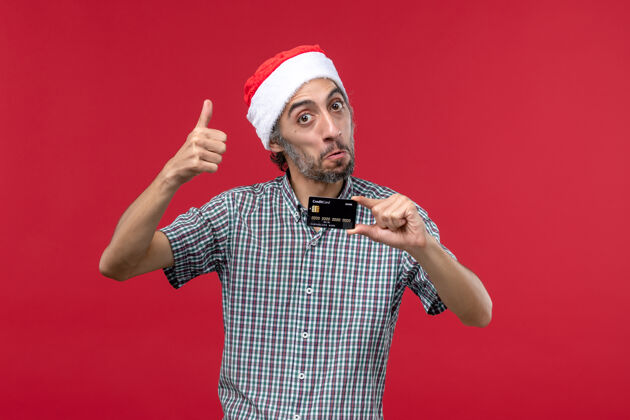 情绪正面图：年轻男性手持红色背景的银行卡钱一圣诞节