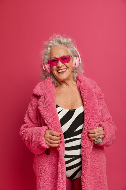 聆听穿着粉色紧身衣和外套 满脸皱纹的时尚老奶奶的特写照片娱乐音乐快乐