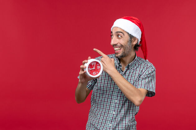 人正面图红色背景上手持圆形时钟的年轻男性前面圣诞节男性