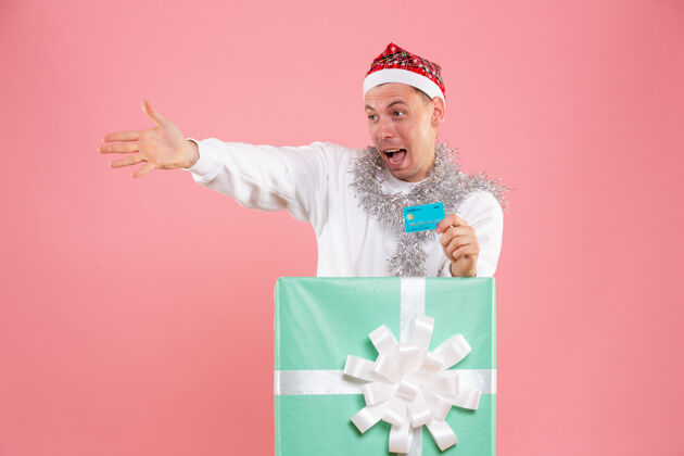 银行正面图里面的年轻男性手持粉色背景的银行卡粉色圣诞节礼物