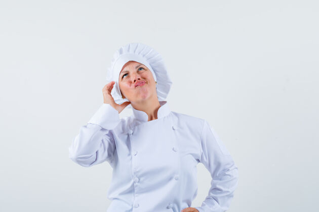 魅力女厨师摆出像在打电话一样的姿势 穿着白色制服思考 看起来很专注而嘴唇电话