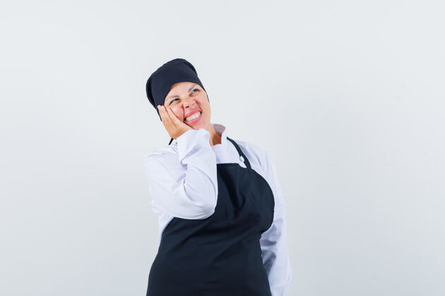黑色金发女人站在思考的姿势 脸靠在手上 身穿黑色厨师制服 看起来沉思模特时尚可爱
