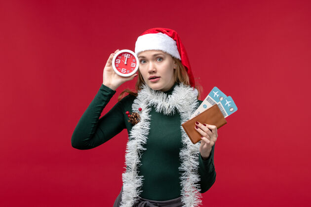 人正面图红色背景上手持时钟和门票的年轻女性时钟姿势圣诞节