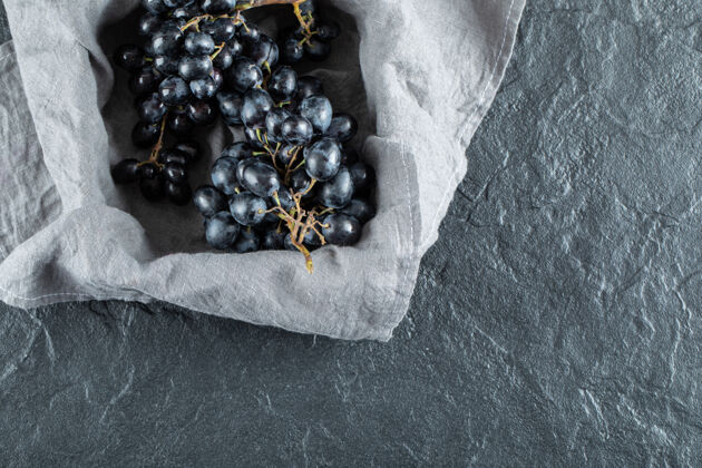 黑色在灰色桌布上的篮子里放着新鲜的黑葡萄有机成熟美味