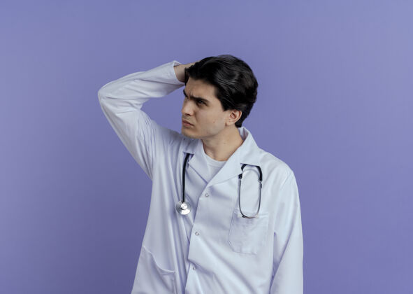 头困惑的年轻男医生穿着医用长袍和听诊器 手放在头上 看着隔离在紫色墙壁上的一边 还有复印空间手年轻看