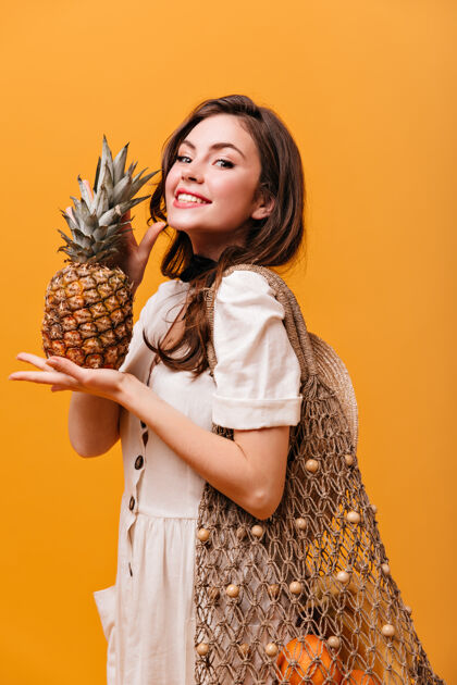 肖像乐观的女人拿着一个大环保袋 手里拿着菠萝 在橙色的背景下微笑着线包女性年轻人