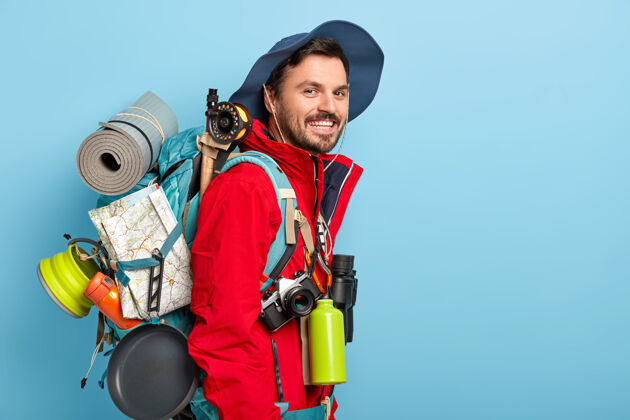 男人微笑的男游客戴着帽子和红色夹克 背着带地图的背包 穿着卡雷马特 用望远镜 烧瓶和热饮爱好请徒步旅行