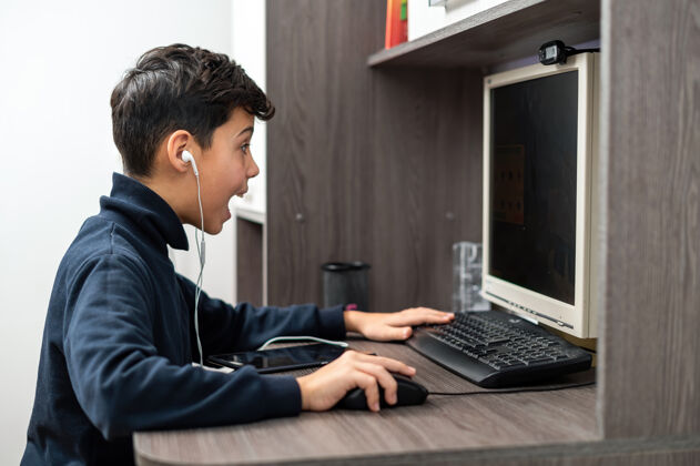 知识男孩正在用带耳机的电脑高兴和兴奋的脸Pc室内笔记本电脑