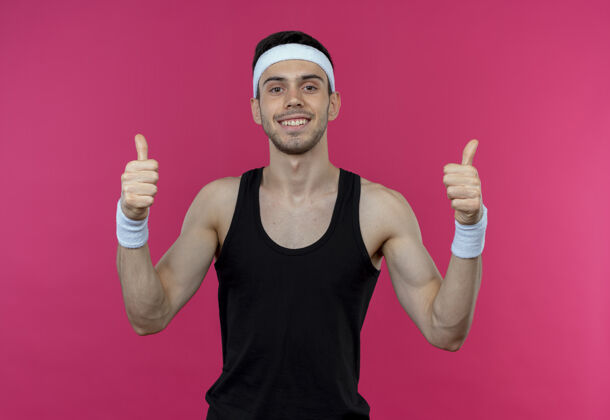 站戴着头巾的年轻的运动型男人微笑着快乐而积极地向粉色竖起大拇指男人年轻快乐