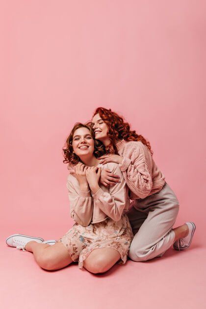 友谊情绪化的漂亮女孩坐在粉色背景上两个朋友在地板上合影拥抱快乐粉色女性