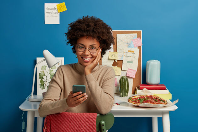 高兴快乐的黑皮肤女孩享受免费高速互联网 用手机发短信 坐在办公室对面女性工作场所年轻人