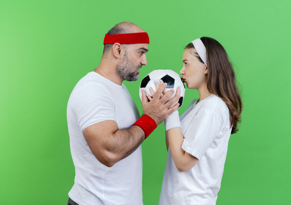 长相一对戴着头带和腕带的成年运动情侣给男人留下了深刻的印象 两个男人都拿着足球 女人亲吻着球看着对方每个女人情侣
