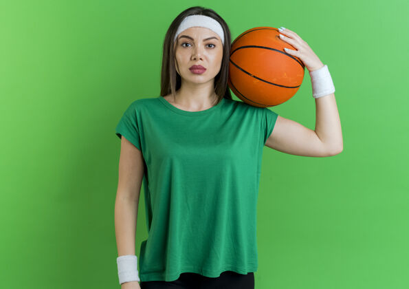球自信的年轻运动女性戴着头带和腕带肩上拿着篮球看头带期待运动