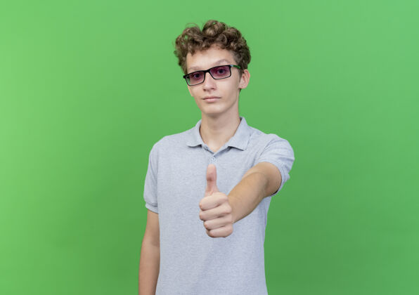 马球戴着黑眼镜的年轻人 穿着灰色马球衫 面带微笑 积极地向绿色竖起大拇指穿站看