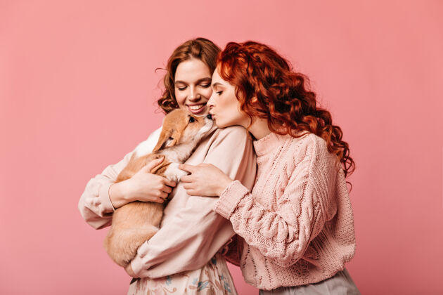 粉色姜女亲吻粉红色背景上的狗摄影棚拍摄惊人的女孩与小狗合影友谊年轻成人