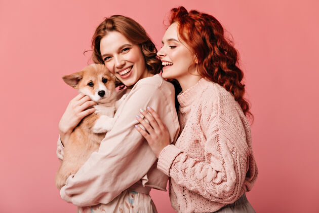 卷发美丽的女孩抱着可爱的狗在粉红色的背景下孤立微笑的欧洲妇女与宠物合影工作室拍摄宠物狗粉色