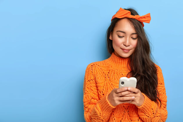 蝴蝶结穿着橙色毛衣的年轻女子在智能手机上聊天电子编织博客