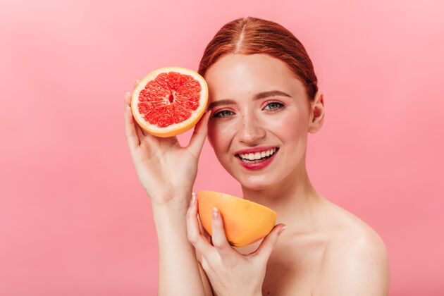 表情神奇的高加索女孩拿着切好的葡萄柚摄影棚拍摄的美丽裸体女人和柠檬在粉红色背景上摆姿势孤立的粉色一个人生姜