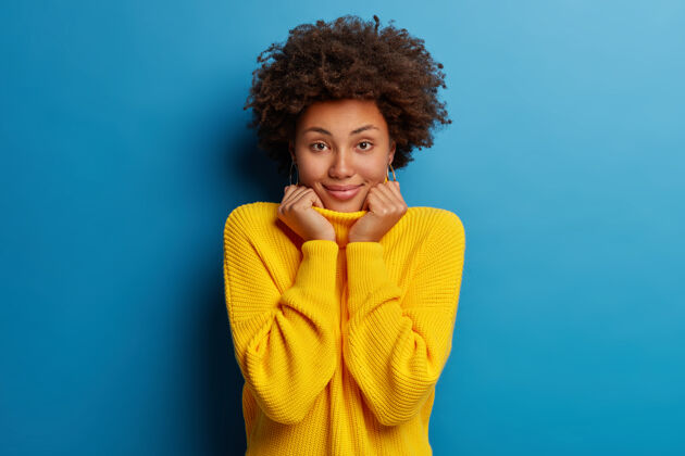 衣领积极的美国黑人年轻女子笑容满面 身穿黄色套头衫 背景为蓝色个人年轻快乐