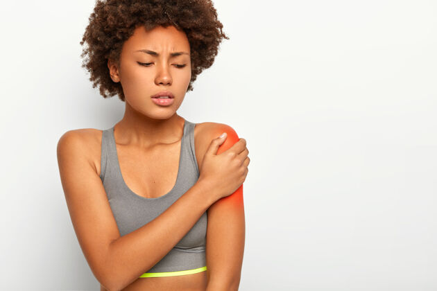 疼痛不满意的非洲女人摸红肩膀 在运动训练中伸展肌肉 表情悲伤 戴灰色胸罩皮肤成人僵硬