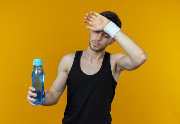 抱着戴着头巾的年轻人手拿一瓶水 站在橘色的墙上感到疲倦感觉瓶子疲劳