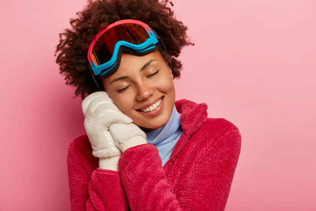 快乐冬季乐趣 休闲和生活方式的概念深色皮肤的女人戴着滑雪板眼镜 双手戴着白手套 回忆着假期的愉快时刻手套乐观欢呼
