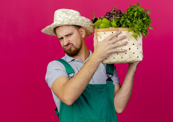 人年轻英俊潇洒的斯拉夫园丁穿着制服 戴着帽子 抱着菜篮子近头望去男人不愉快蔬菜