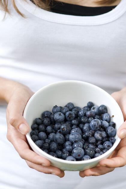 给予拿着装满蓝莓的碗的年轻女人展示单一对象水果
