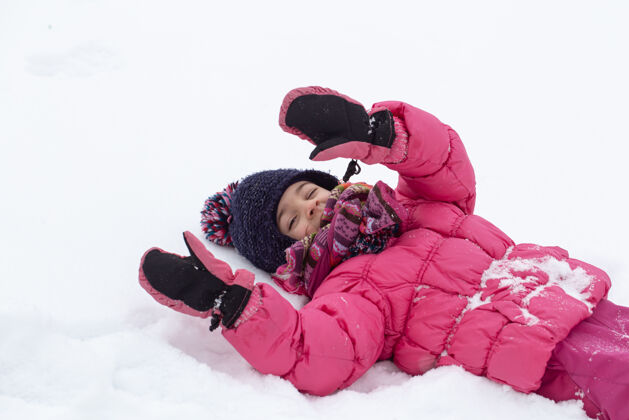天使一个穿着粉色夹克 戴着帽子的可爱小女孩正在雪地里玩耍冬季儿童娱乐理念自然孩子乐趣