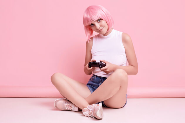 情感美丽快乐的游戏女孩与粉红色头发的肖像玩游戏机上五颜六色的操纵杆在工作室霓虹灯游戏生动