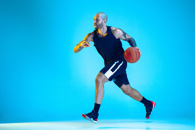 活跃年轻的篮球队员穿着运动服训练 在运动中练习 运动在霓虹灯下隔离在蓝色的墙上运动的概念 运动 活力和活力 健康的生活方式男子运动男性