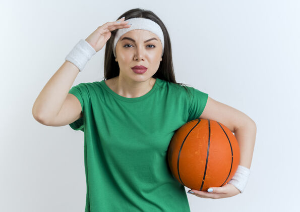抱自信的年轻运动女性戴着头带和腕带拿着篮球遥望远方女子球看
