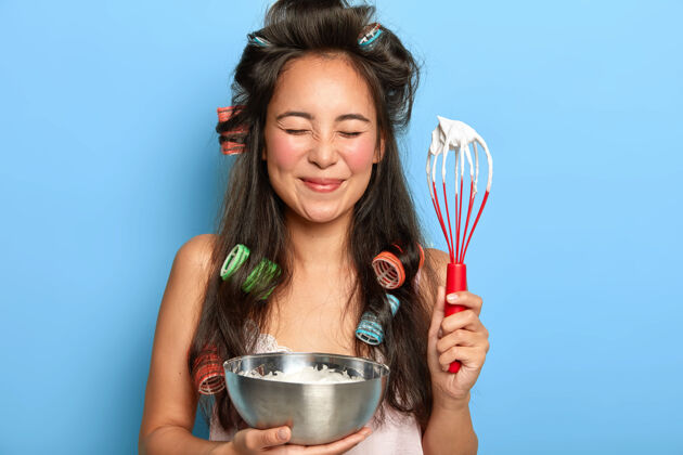 烹饪满意的黑发女人在碗里搅拌酸奶油 戴着卷发器穿产品女性